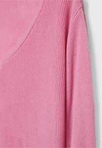 Pull rose tricoté avec un col en V, présentant une texture côtelée et un tissu de poids moyen. La manche est légèrement ample.