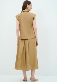 Tan, knælang kjole med tætsiddende bodice, kapærmer og plisseret nederdel. Glat tekstur, minimalistisk design og en subtil glans.