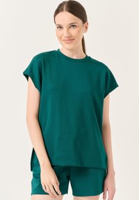 Teal gebreide top met korte mouwen, ronde halslijn en zijsplitten, gecombineerd met bijpassende shorts. De stof lijkt zacht en ademend te zijn.
