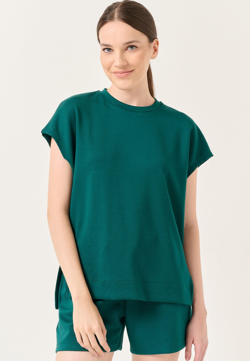Teal gebreide top met korte mouwen, ronde halslijn en zijsplitten, gecombineerd met bijpassende shorts. De stof lijkt zacht en ademend te zijn.