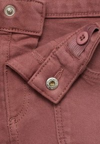 Rautan värinen kangas, jossa on sileä tekstuuri, napin kiinnitys, hopeiset tarvikkeet ja yksityiskohtainen ompelu. Koristeita ovat napilla varustettu väli.