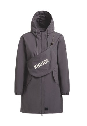 Junge Frau mit gekreuzten Beinen, die eine graue Kapuzenjacke, ein schwarzes Crop-Top, schwarze Leggings und schwarze robuste Stiefel trägt.