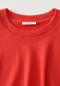 Sudadera de algodón roja con cuello redondo acanalado, que presenta una textura suave y una etiqueta de logo que muestra "OPUS" en el interior del cuello.