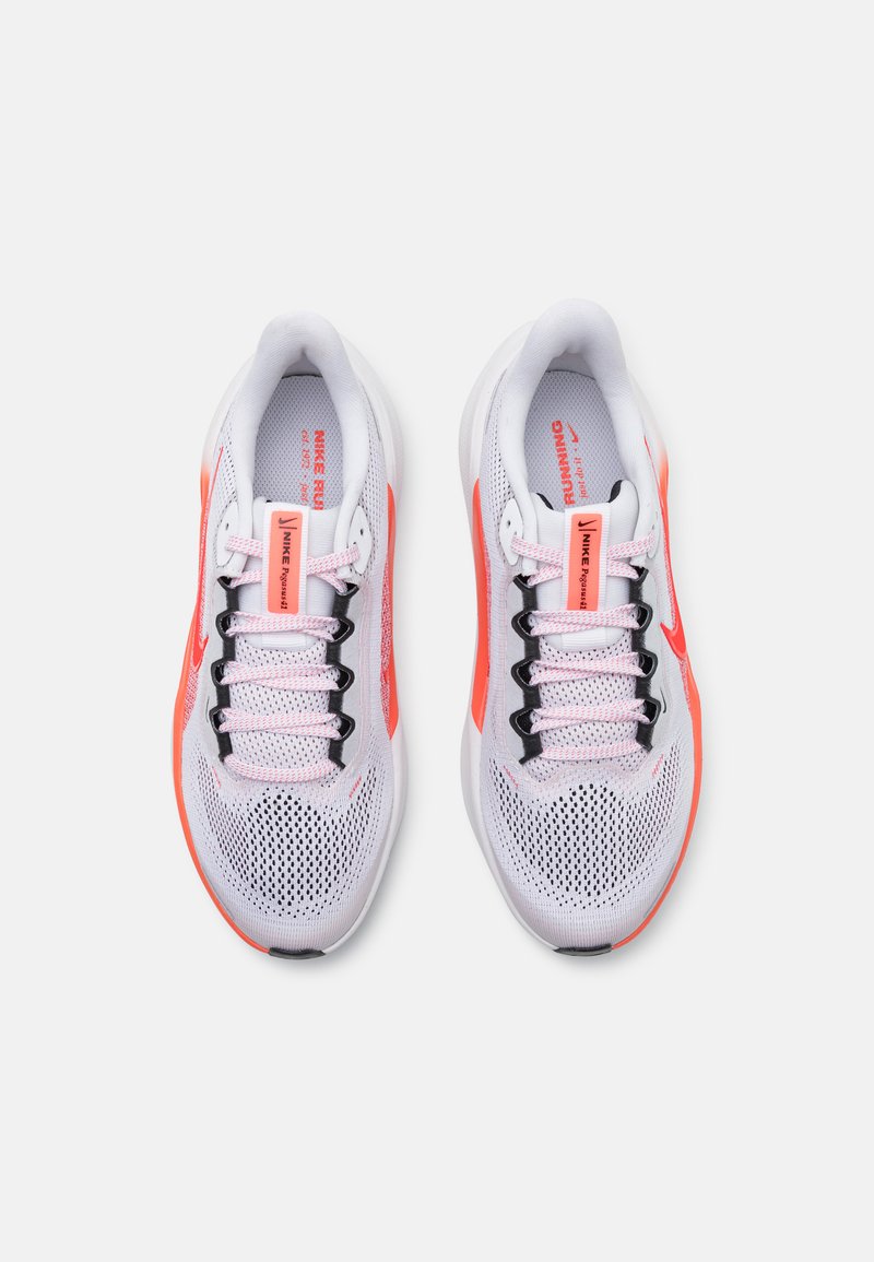 Zapatillas de running Nike de malla blanca con acentos en coral. Presentan cordones negros, lengüeta acolchada y una construcción transpirable. Diseñadas para la comodidad.