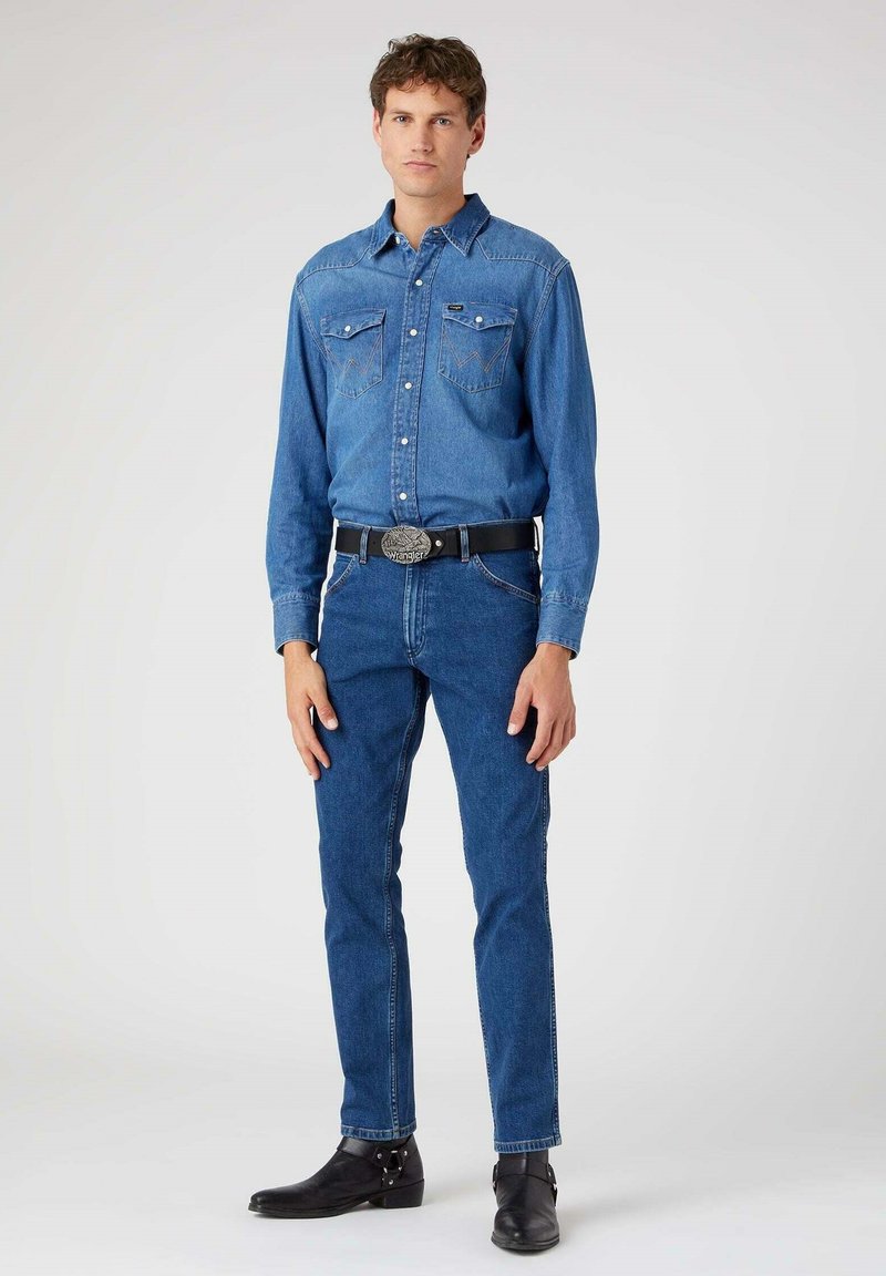 Denim shirt in light blue with snap buttons and two chest pockets, paired with dark blue slim-fit jeans and black ankle boots.