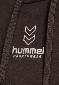 Hoodie marron avec une texture douce, ornée d'un logo blanc brodé et de deux motifs en chevron sur le devant. Comprend des cordons assortis.
