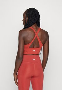 Rød atletisk crop top med krydset rygdesign, lavet af strækbart stof, parret med højtaljede leggings med logo-detaljer.