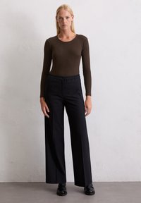 Bruin geribbeld langslavend shirt en wijde zwarte broek met hoge taille. Zwarte schoenen maken de outfit compleet. Eenvoudig en aansluitend ontwerp.