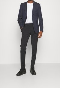 Granatowa marynarka z dwoma przednimi kieszeniami, połączona z ciemnoszarymi spodniami i czarnymi trampkami. Stylizacja zawiera białą koszulkę z okrągłym dekoltem pod spodem.