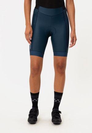 Shorts da ciclismo blu navy realizzati in un tessuto liscio ed elastico, dotati di una seduta imbottita e un cintura nera a contrasto. Indossati con calze e scarpe nere.
