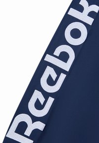 Granatowa odzież sportowa z dużym, białym haftowanym logo "Reebok" po boku. Gładka faktura, nowoczesny design i czyste linie.