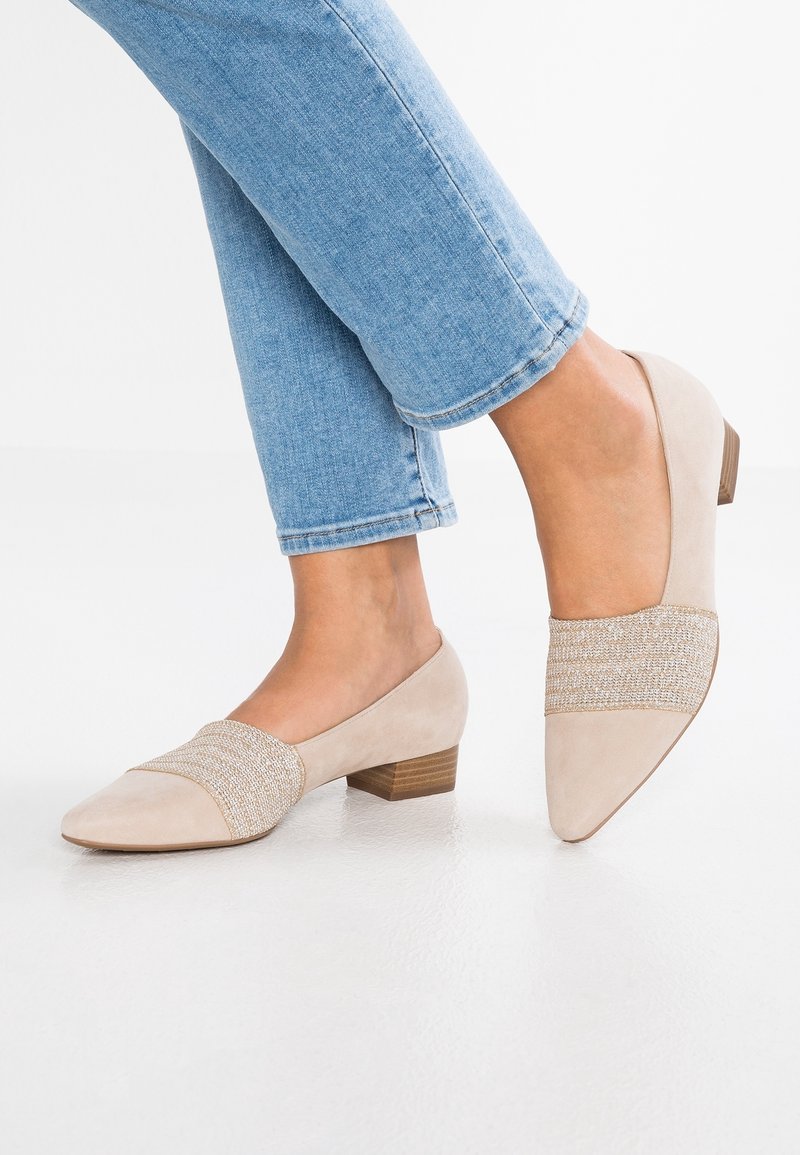 Chaussures plates beiges avec un panneau en tissu texturé, un bout pointu et un petit talon en bois. Le dessus présente du daim lisse et des détails tissés.