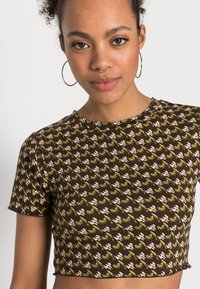 Brown cropped t-shirt featuring a textured pattern in green and cream, with a round neckline and short sleeves. Smooth, stretchy fabric.