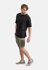T-shirt nera a maniche corte abbinata a pantaloni cargo khaki. Modello che indossa sneaker grigie chiare. Abbigliamento semplice e casual.