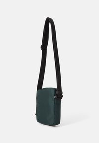 Grøn nylon skuldertaske med rektangulær form, sort justerbar rem og minimalistisk design. Har diskret syninger og hardware-detaljer.
