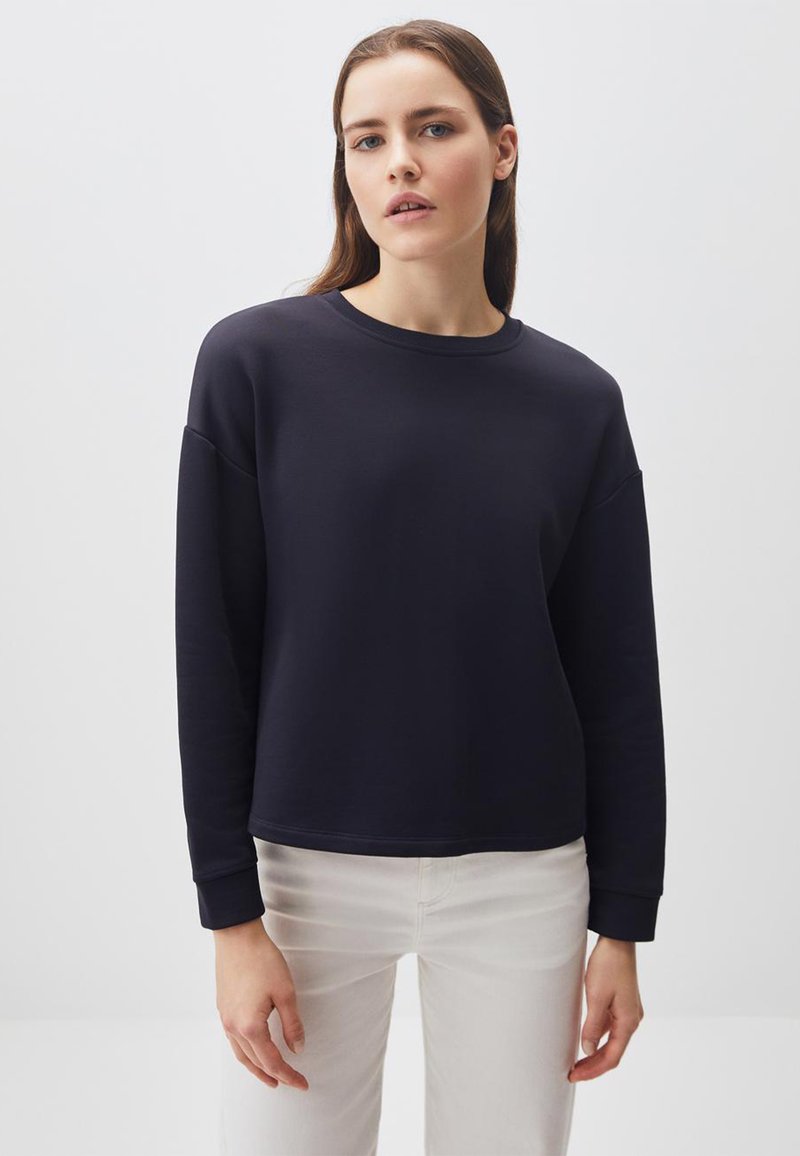 Felpa blu navy con girocollo, spalle basse, maniche lunghe e polsini a costine. Tessuto liscio, abbinata a pantaloni chiari.