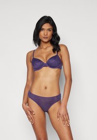 Lila melltartó texturált mintával és állítható pántokkal, amelyhez hasonló mintázatú és puha szélekkel rendelkező, illeszkedő bikini alsórész tartozik.