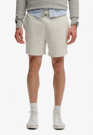 Man draagt lichtgrijze shorts met trekkoord, witte crew-sokken, witte sneakers, een grijze trui en eronder een blauw gestreept overhemd.
