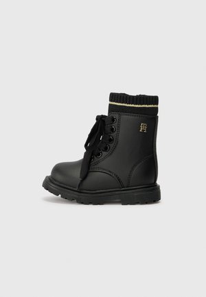 Bottines noires en simili cuir lisse, avec un col en tricot noir côtelé et une bande dorée, fermeture à lacets et semelle en caoutchouc épaisse.