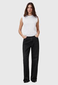 Weißes ärmelloses Oberteil und hoch taillierte schwarze Jeans mit geradem Bein. Die Jeans haben einen ausgefransten Saum und seitliche Taschen.