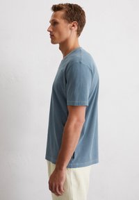 T-shirt en coton bleu à manches courtes, col rond et coupe décontractée. Détail de fente latérale notable à l'ourlet.
