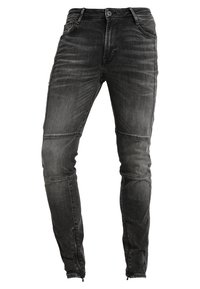 Jeans ajustados en denim negro deslavado, con detalles de cremallera en los tobillos, ligero desgaste y un acabado ligeramente desgastado.