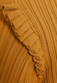 Pull en maille jaune moutarde avec des côtes verticales et un bord froncé sur un côté, mettant en valeur une surface texturée et un tissu élastique.