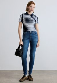 Tengerészkék és fehér csíkos galléros póló, magas derekú kék farmernadrággal párosítva. Fekete kis kézitáska és leopárdmintás cipők teszik teljessé a megjelenést.