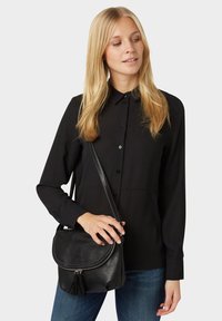 Camisa negra de manga larga con cierres de botón, combinada con un bolso de piel negro tipo bandolera con detalle de borlas y una correa para el hombro.