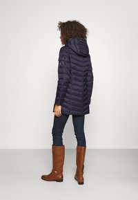 Granatowa kurtka puchowa z kapturem, z pikowanym wzorem. W połączeniu z ciemnymi dżinsami i brązowymi, wysokimi botkami do kolan z złotym akcentem.