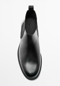 Bottes basses en cuir noir avec panneaux latéraux élastiques, bout légèrement pointu, texture lisse et une boucle pour faciliter l'enfilage, dotées d'une semelle plate.