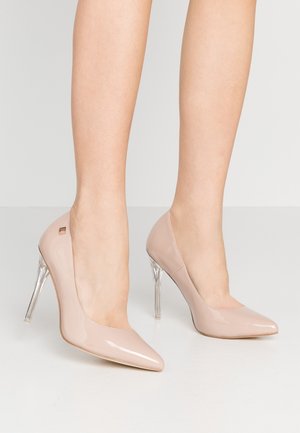 Nude patentlæder højhælede sko med spids tå og gennemsigtig stilettohæl. Glat tekstur og diskret brandingdetalje bagpå.