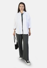 White button-up shirt, dark green top underneath, gray wide-leg trousers, black handbag, and black sneakers with white soles.