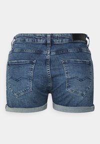 Shorts de mezclilla con un lavado azul medio, dobladillos enrollados y dos bolsillos traseros con un patrón de costura en forma de ola. Parche de cuero con el logo en la cintura.