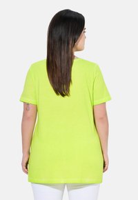 Lys grøn kortærmet t-shirt, blød tekstur, afslappet pasform, rund halsudskæring, længere bagkant, båret med hvide bukser.
