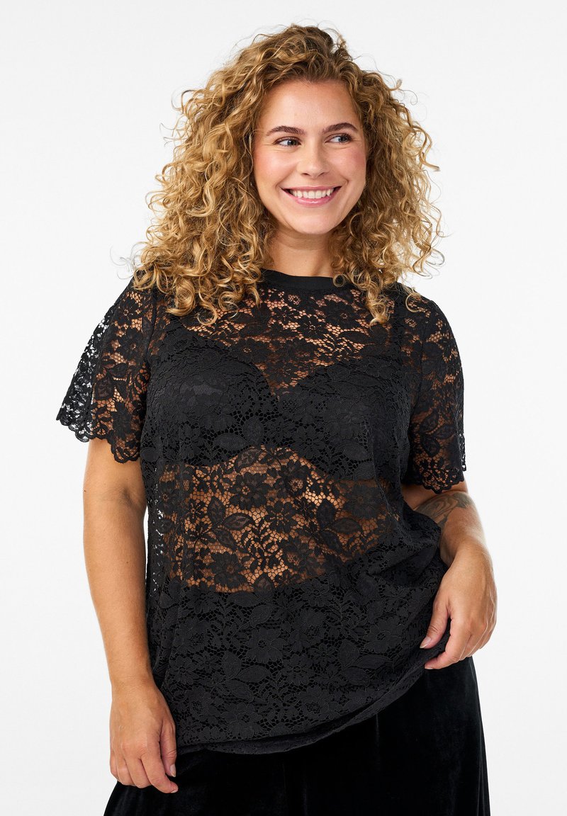 Top in pizzo nero con maniche corte, caratterizzato da motivi floreali e un design semi-trasparente. Texture liscia e scollatura rotonda.