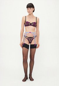 Zestaw bielizny z czarnej i fioletowej koronki, zawierający biustonosz typu balconette, dopasowany stringi oraz pas do pończoch z niebieskimi paskami i różowymi akcentami.