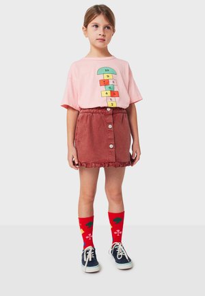Pink cotton t-shirt with hopscotch design, rust-colored corduroy skirt with button details, red socks with colored shapes, navy shoes.