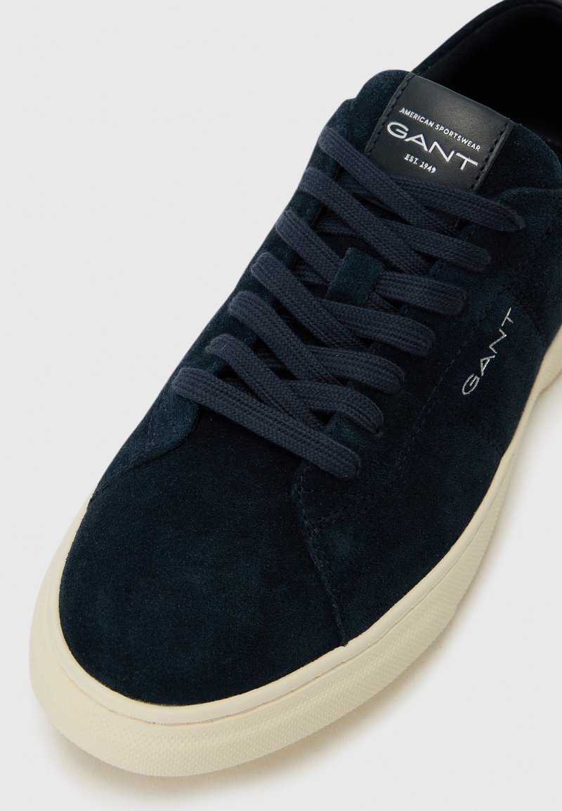 Sneaker in suede blu navy con punta rotonda, chiusura con lacci e suola in gomma beige. Presenta una parte superiore testurizzata e una linguetta in pelle con il marchio.