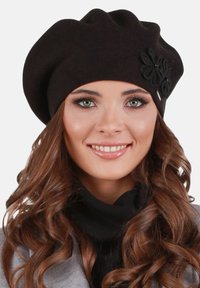 Černá bereta vyrobená z měkké látky, s dekorativním květem na boku. Zaoblený tvar a strukturovaný povrch pro komfort a styl.