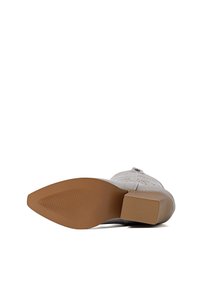 Stivaletto beige con tomaia testurizzata e perforazioni, punta quadrata e suola in gomma marrone con motivo a righe per una presa migliore.