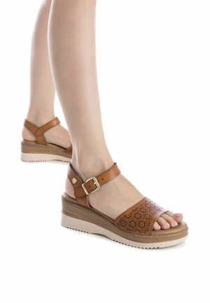 Sandalias de cuña de cuero marrón con diseño perforado, tira adjustable en el tobillo y suela texturizada. Con un tacón de madera y suela de color claro.