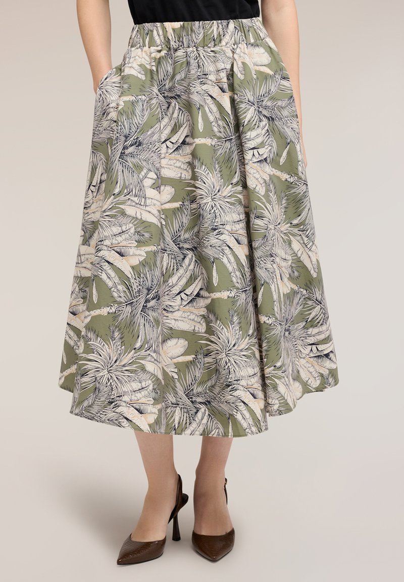 Woman wearing olive green midi skirt with white and black tropical leaf print and brown pointed high heels.