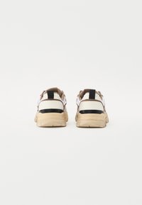 Sko med en kraftig beige s�åle, overdel i hvitt og brunt nettstoff, svart lærdetalj, og en løkke på hælen for enkel påkledning.