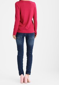Maglione fucsia a maniche lunghe con scollatura rotonda, abbinato a jeans skinny blu e scarpe con tacco rosa chiaro, visto da dietro.