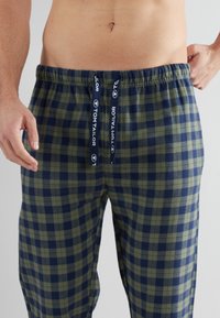 Pantalons de pyjama à carreaux en vert foncé et bleu marine, en tissu doux. Comprend une taille élastique avec cordon de serrage et des accents de marque. Coupe décontractée.