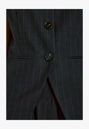 Dark blue pinstripe suit fabric featuring two glossy black buttons, tailored cut with sharp lapels and slim pockets. Stitching accents visible.