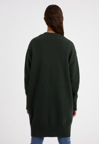 Mörkgrön oversized tröja med långa ärmar, rundad halsringning och ribbade muddar, som sträcker sig nedanför höfterna, tillverkad i ett mjukt texturerat material.