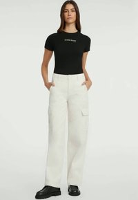 T-shirt preto ajustado com o logótipo "GUESS JEANS", combinado com calças cargo brancas com bolsos laterais e design de perna larga. Calçado chunky preto.