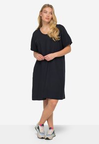 Černé šaty až ke kolenům s krátkými nabíranými rukávy, kulatým výstřihem a volným střihem. Oblečené s vícebarevnými sportovními teniskami.